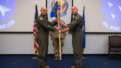U.S. Air Force Col. Joshua M. Biedermann, left, 53rd Test and Evaluation Group commander, passes the unit guidon to Lt. Col. Matthew W. Jensen, inaugural commander of the Experimental Operations Unit (EOU), during the EOU activation ceremony at Nellis Air Force Base, Nevada, June 5, 2025. The transfer of the guidon formally established the new unit under Jensen’s leadership. (U.S. Air Force photo by Airman 1st Class Michael Sanders)
